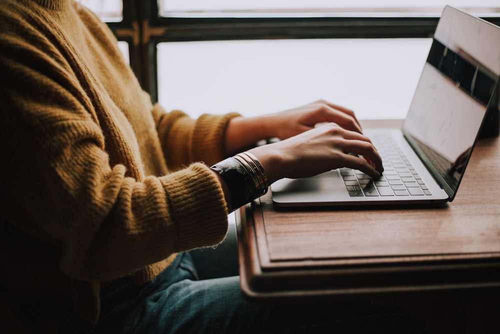 A writer typing on a laptop by a window